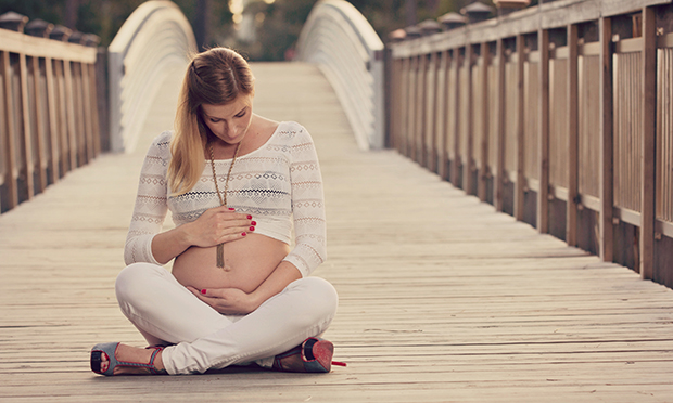 Jovem grávida, sentada, com as mãos na barriga.