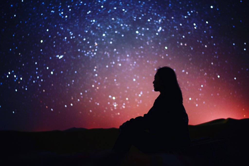 Foto de silhueta de uma pessoa sentada diante de um céu estrelado