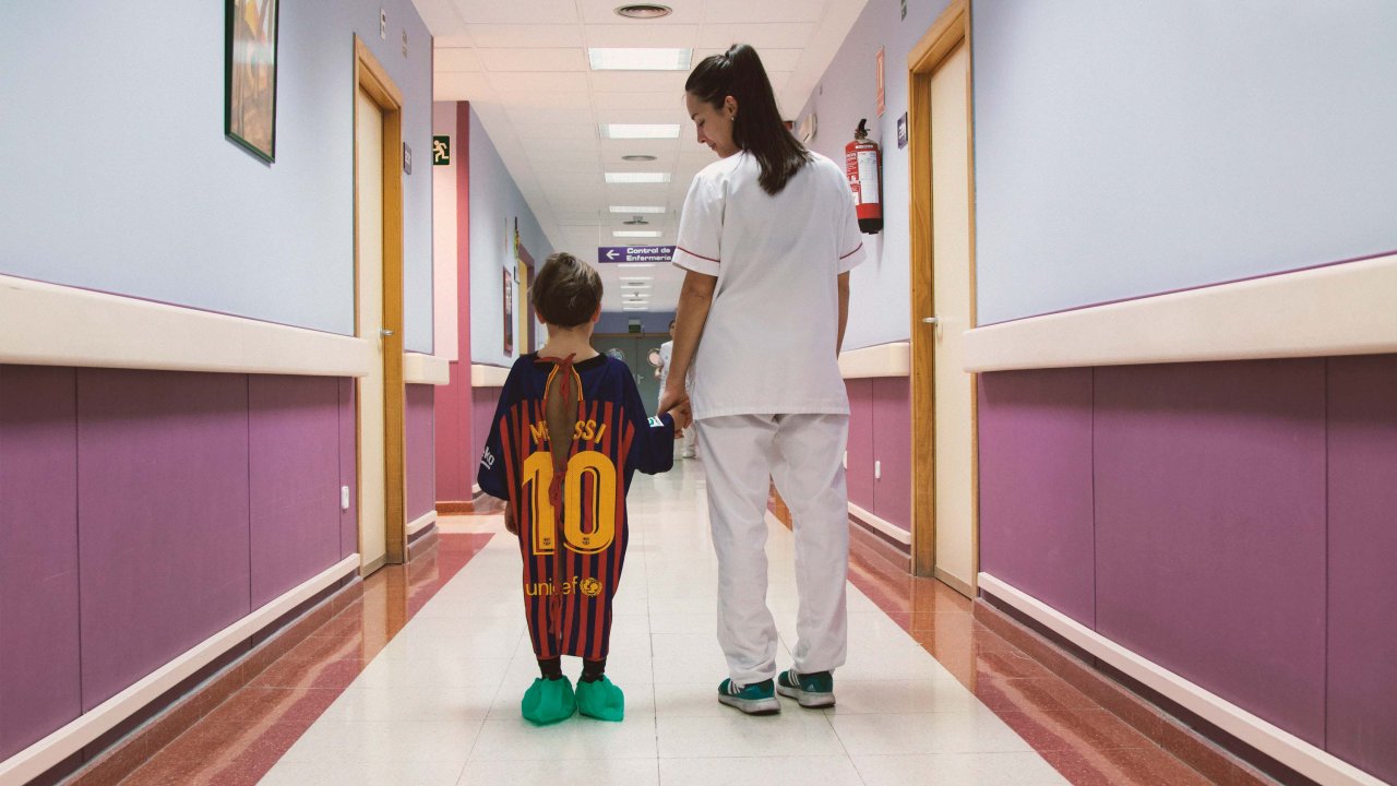 Enfermeira e criança usando camisa de time como bata hospitalar em corredor de hospital na Espanha