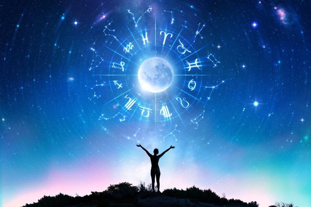 silhueta de mulher olhando a lua cheia e os signos do zodíaco no céu