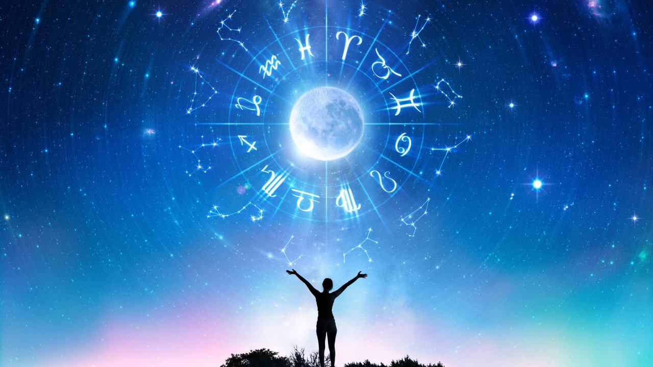 silhueta de mulher olhando a lua cheia e os signos do zodíaco no céu