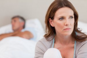 Sad mature woman on bed with her husband in the background