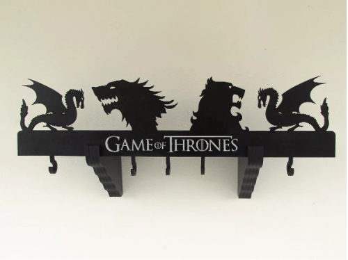 Prateleira/Cabideiro Game Of Thrones, de MDF, nas medidas <span>65 x 20 x 18 cm</span>. <a href="https://produto.mercadolivre.com.br/MLB-1149276079-prateleira-cabideiro-game-of-thrones-got-mdf-_JM?matt_tool=10496100&matt_word&gclid=EAIaIQobChMIyJfIieKi4QIVD1cMCh1DnQLsEAkYDSABEgI96PD_BwE&quantity=1" target="_blank" rel="noopener">Mercado Livre</a>, R$ 159,90