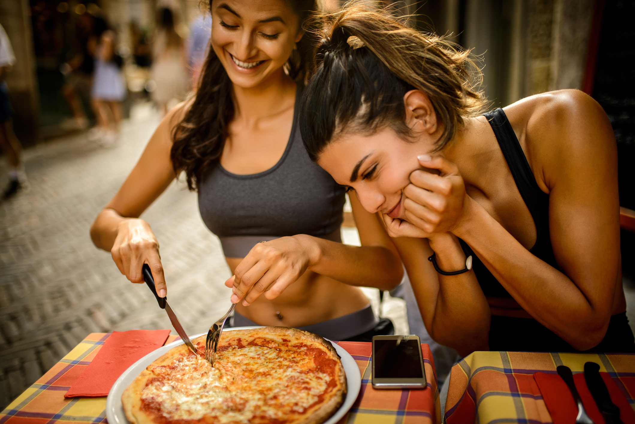 Sporty woman eating pizza while her friend looking at it MStudioImages/Gett...