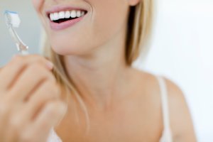 Smiling woman brushing teeth, cropped
