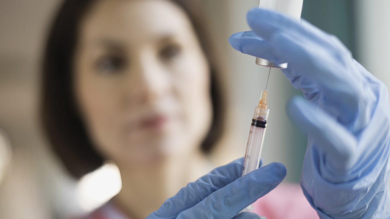 Mulher usando seringa para retirar dose de vacina de um frasco