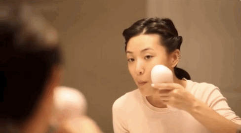 japonesa se olhando no espelho enquanto massageia o rosto