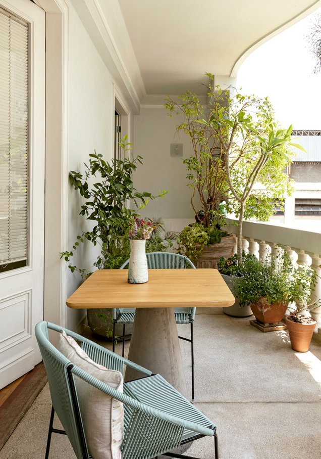 Na varanda, mesa com base de concreto e cadeiras de aço e PVC da Cremme.