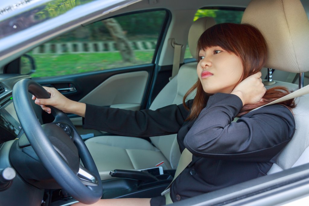 Young woman massaging her neck or shoulder while driving a car after long hour - pain concept