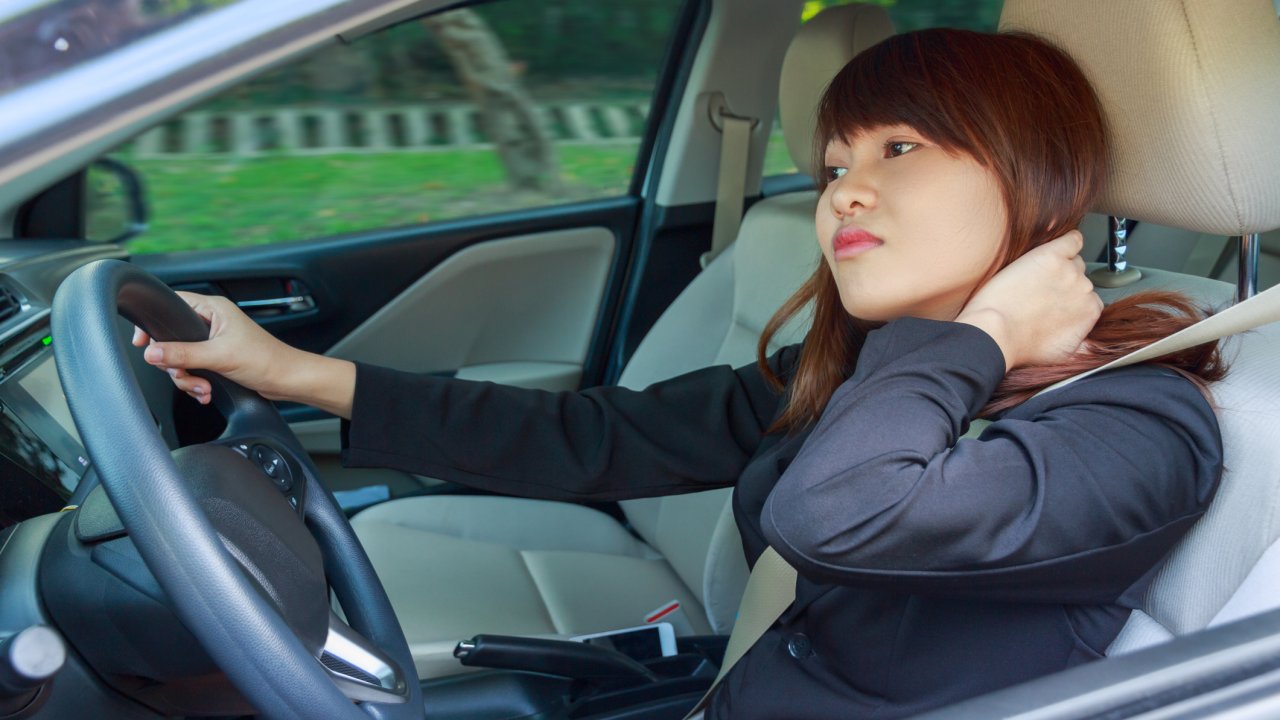 Young woman massaging her neck or shoulder while driving a car after long hour - pain concept