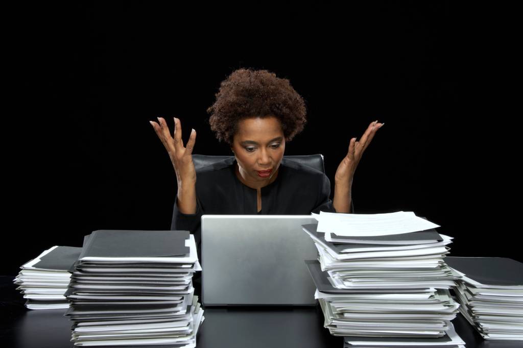 Businesswoman at desk by laptop and paperwork, hands raised