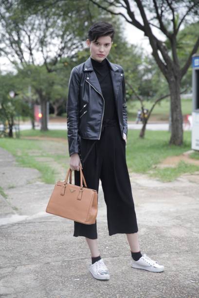 Os tênis brancos e a bolsa de tons terros quebram o look total black