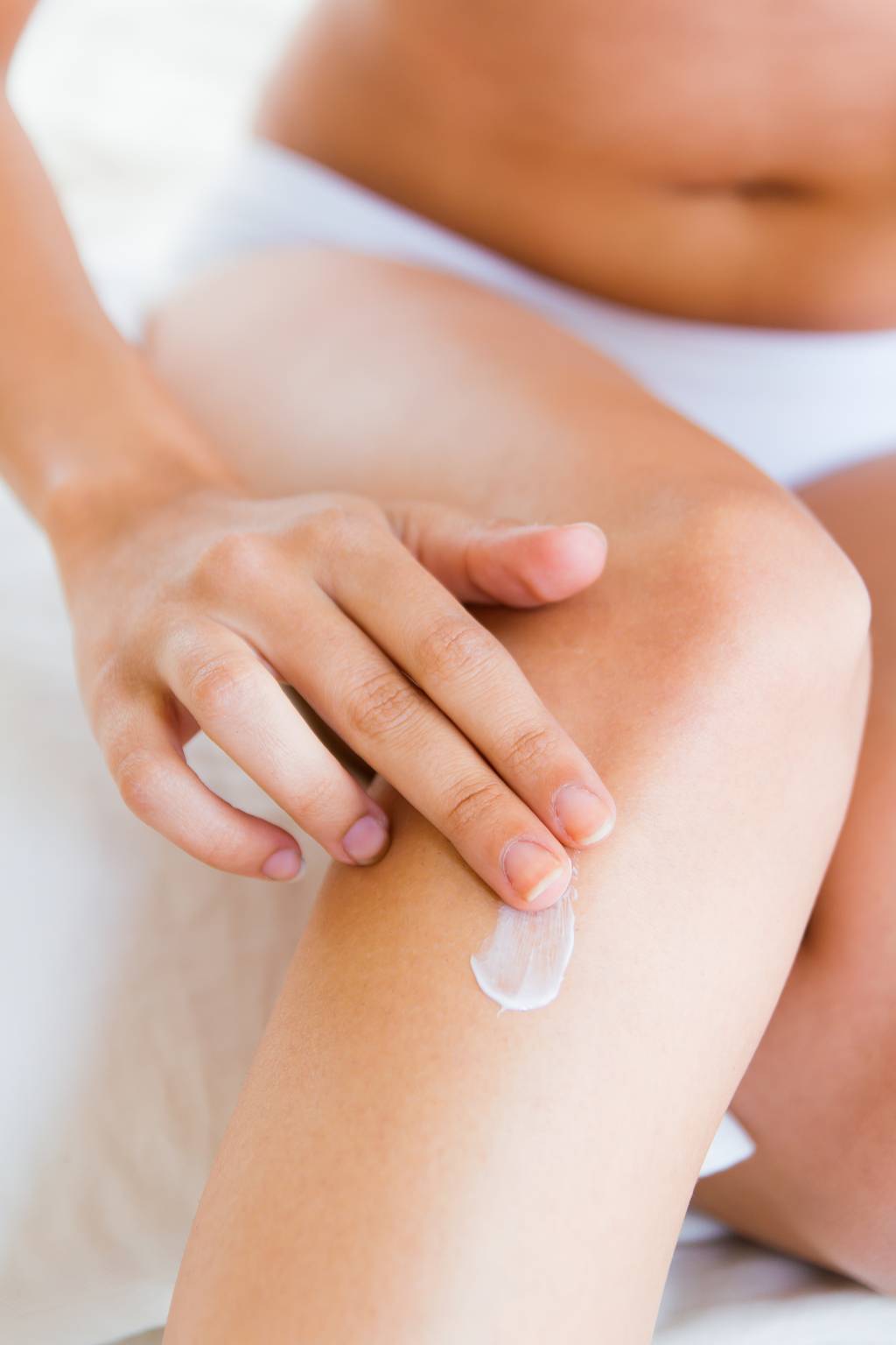 Cuidados com joelhos e cotovelos no frio Pretty young woman caring about her legs with moisturizing cream