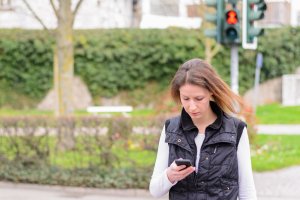 Mulher atravessa a rua enquanto olha o celular
