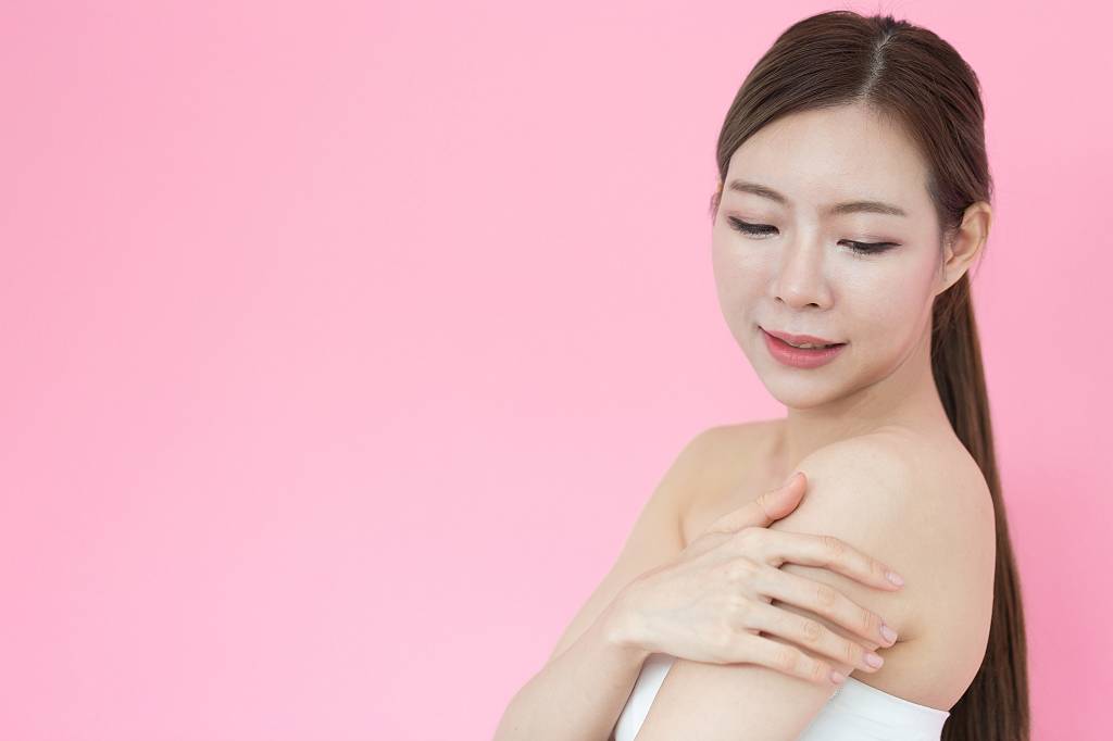 Como adaptar o ritual de beleza das coreanas à realidade brasileira? Beautiful Asian woman touching shoulder and smile with healthy skin,Isolated on pink background