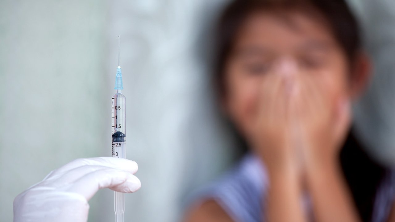 Close up doctor hand holding syringe with a child girl fear to receive vaccine injection background