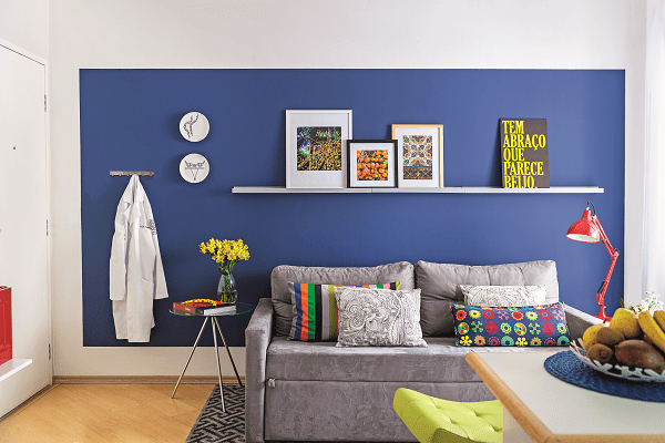 <span>A estrela da sala é a parede azul – note que ela não é inteiramente tingida, funcionando como um painel pintado. Neto dá as dicas para copiar: “A referência para a altura deve ser a porta ou uma viga, o que estiver mais visível para equilibrar o alinhamento. Já para as laterais e a parte de baixo, sugiro afastamento de 15 a 20 cm”. A proposta valoriza a superfície sem deixar o ambiente pesado. “Uma saída para quem tem medo de abusar do tom escuro”, aponta o arquiteto. Tintas da sala: painel azul cor Tratamento Real e demais paredes cor Cinza de Grife, da Coral. Acrílico fosco. </span>Projeto do arquiteto Neto Porpino