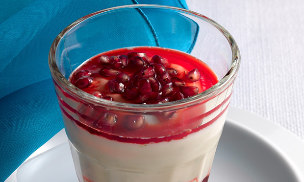 Um creme branco com cobertura vermelha e sementes de romã dentro de um copo de vidro