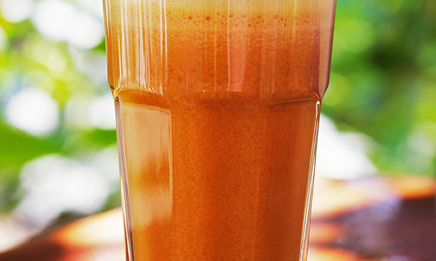 Um copo de suco de cor laranja cheio aparece sobre um fundo desfocado verde
