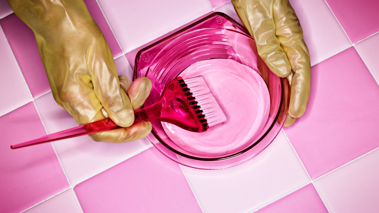 Mãos com luvas rosas preparando tinta para pintar o cabelo