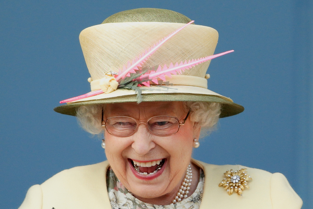 A rainha Elizabeth é uma mulher de cabelos brancos curtos e pele branca. Ela está usando um chapéu verde claro e roupa do mesmo tom. Ela usa colar e brincos de pérola e um broche.