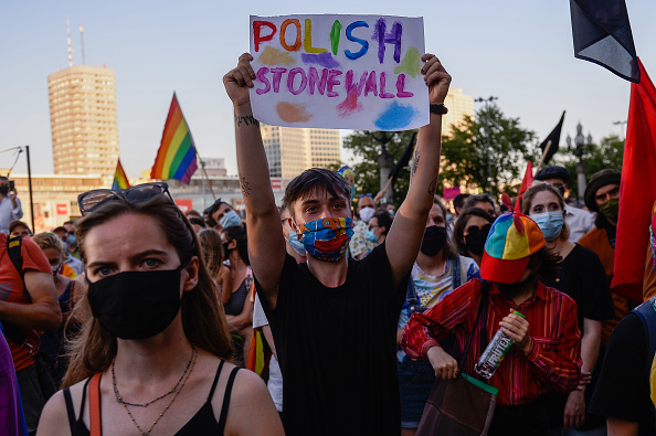 Ativista com máscara protetiva colorida segura ao alto cartaz escrito "Stonewall polonês", em inglês e em letras coloridas.