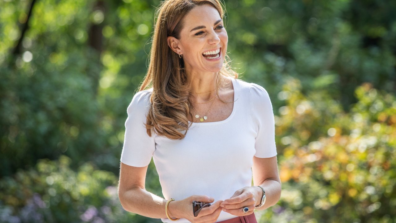 Kate Middleton sorri vestindo camiseta branca