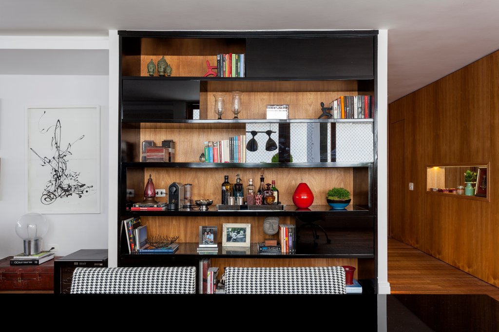 Na foto, aparece estante de madeira com portas pretas. Há vários objetos na estante, como livros, vasos e enfeites