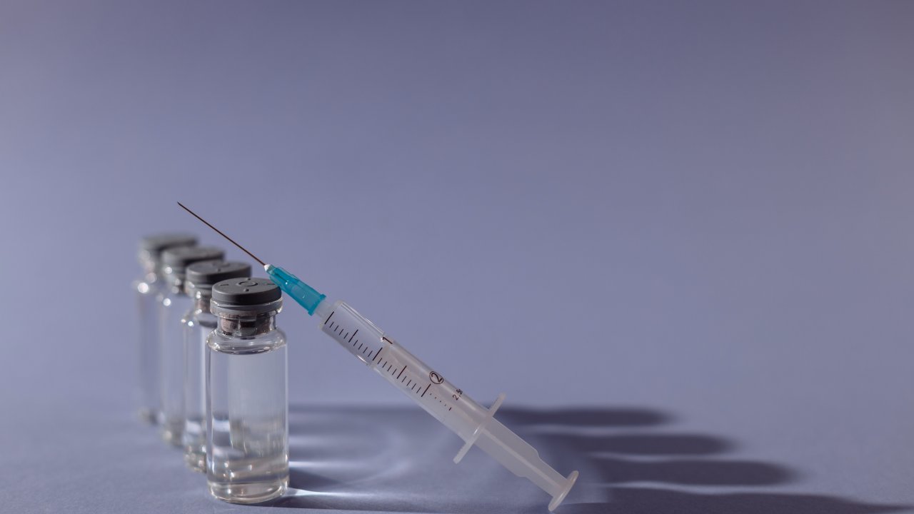 frascos de vacina e uma seringa arrumados contra um fundo lilás