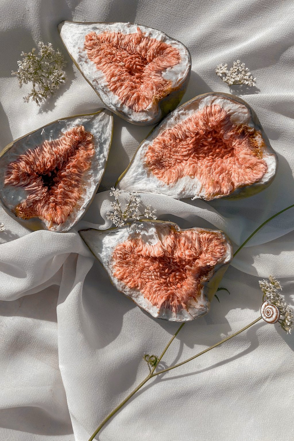 figos cortados ao meio sobre um tecido branco amassado e florzinhas