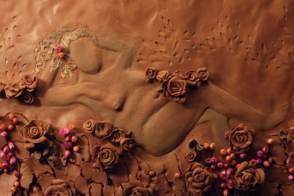 Imagem de um corpo feminino desenhado em argila e cercado por flores
