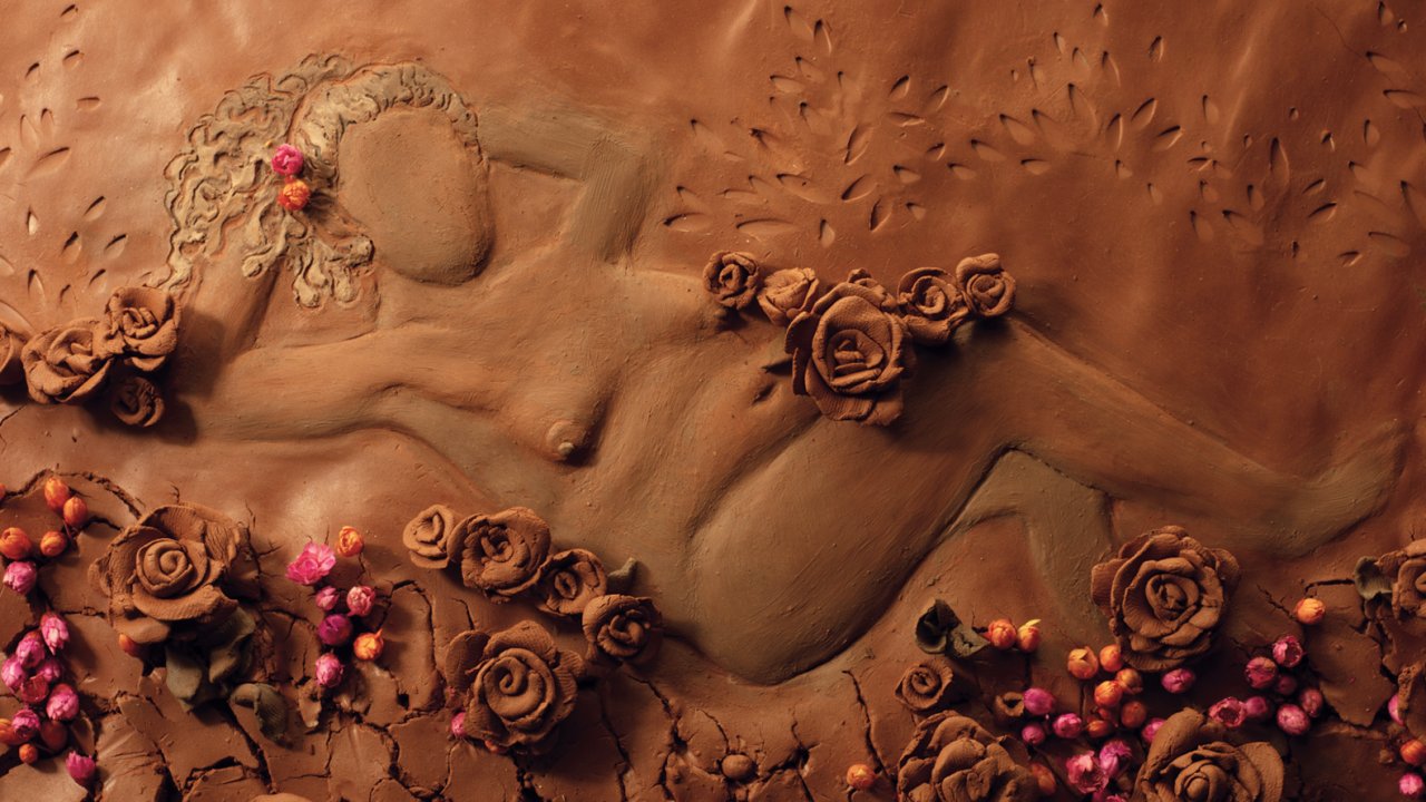 Imagem de um corpo feminino desenhado em argila e cercado por flores