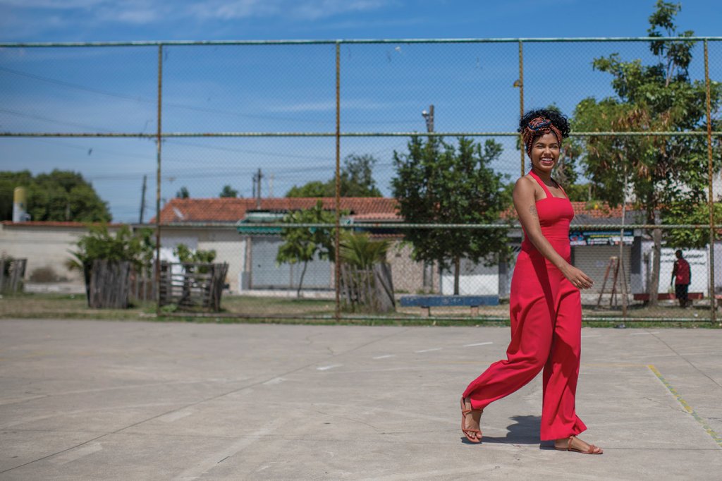 Joyce usa macacão vermelho e caminha por quadra de esportes