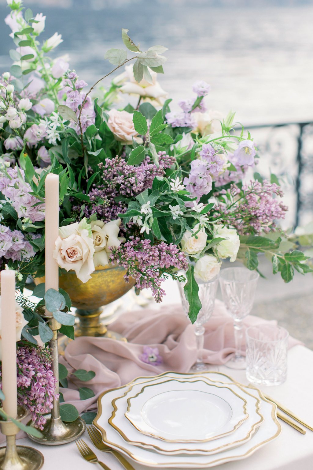 Detalhe da mesa de festa com panos lilás, velas e flores brancas e lilás