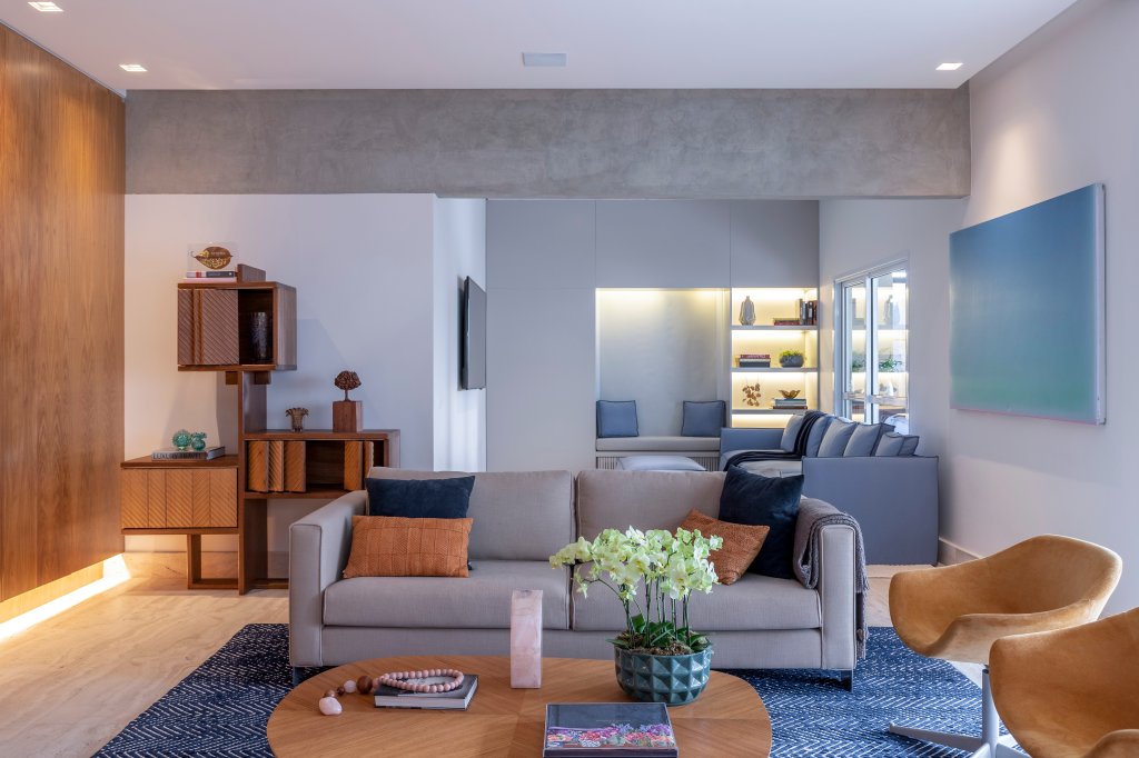Sala de estar integrada com sofá cinza, tapete azul e mesa de madeira