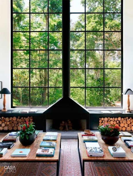 A grande janela com esquadrias pretas, que enquadra o verde da serra fluminense, serve de fundo para a lareira imponente. No projeto do escritório Ouriço Arquitetura, a lenha fica armazenada na própria sala e se torna parte da decoração. A grande janela com esquadrias pretas, que enquadra o verde da serra fluminense, serve de fundo para a lareira imponente. No projeto do escritório Ouriço Arquitetura, a lenha fica armazenada na própria sala e se torna parte da decoração.