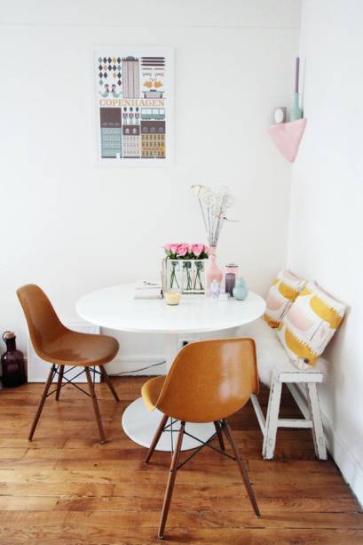 A sala de jantar foi montada com um banco, um par de cadeiras caramelo e uma mesa redonda. Os objetos de decoração em candy colors alegram o ambiente de base neutra.