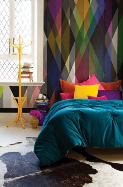 A mistura de cores deste quarto não parou na estampa do papel de parede geométrico: continuou nas almofadas, no edredom e no mancebo amarelo.