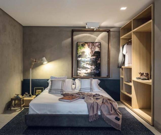 O cimento queimado e um tom de azul profundo predominam na decoração do quarto, aquecida pela mesa de cabeceira e pelo armário, ambos de madeira. Um elemento que chama atenção é o nicho descentralizado, que serve de suporte para a fotografia. O cimento queimado e um tom de azul profundo predominam na decoração do quarto, aquecida pela mesa de cabeceira e pelo armário, ambos de madeira. Um elemento que chama atenção é o nicho descentralizado, que serve de suporte para a fotografia.