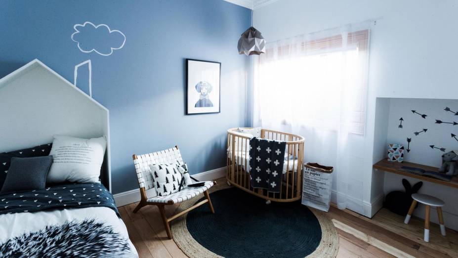 Quarto infantil com parede azul e branca e décor neutro.