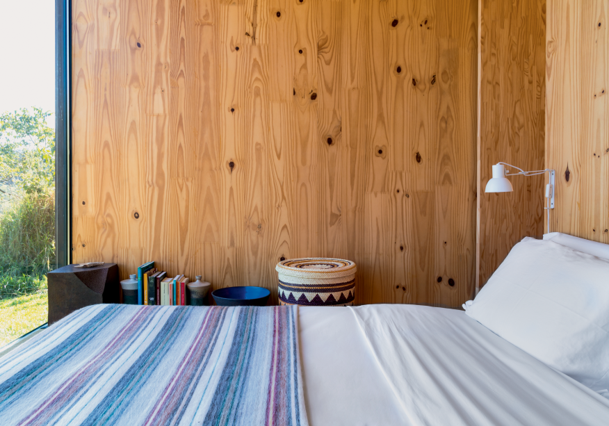 O quarto segue a linha minimalista e confortável e, no lugar da cama, ganhou um colchão sobre o tatame. O vidro ao fundo se estende até a área do boxe, no banheiro.