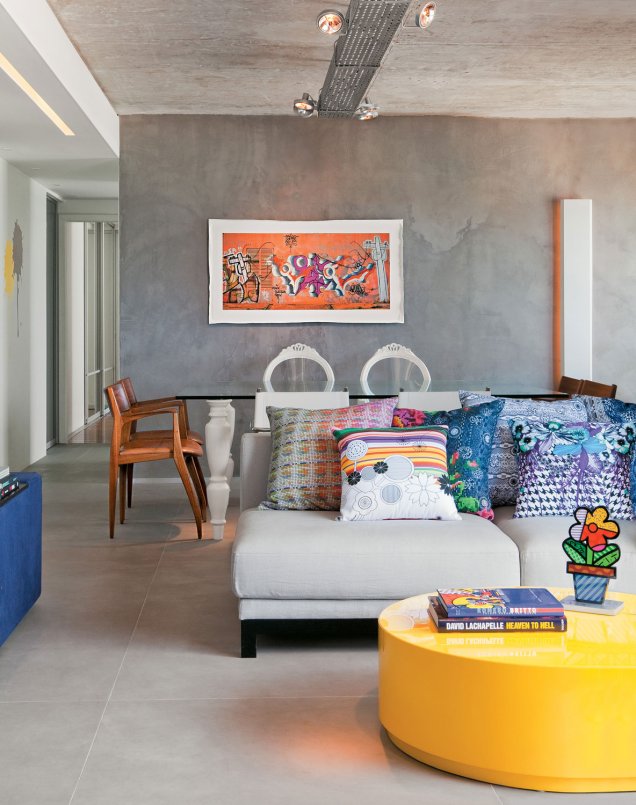 Neste partamento, projetado pelo Arquiteto Carlos Otávio Oliveira, a sala com paredes de cimento ganhou vida com acessórios coloridos e a mesinha de centro amarela.