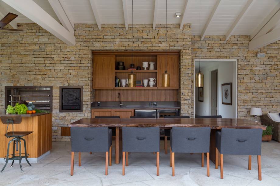 Terraço gourmet, com revestimento de pedra-madeira e mesa de jantar em projeto em estilo provençal do arquiteto Dado Castello Branco.