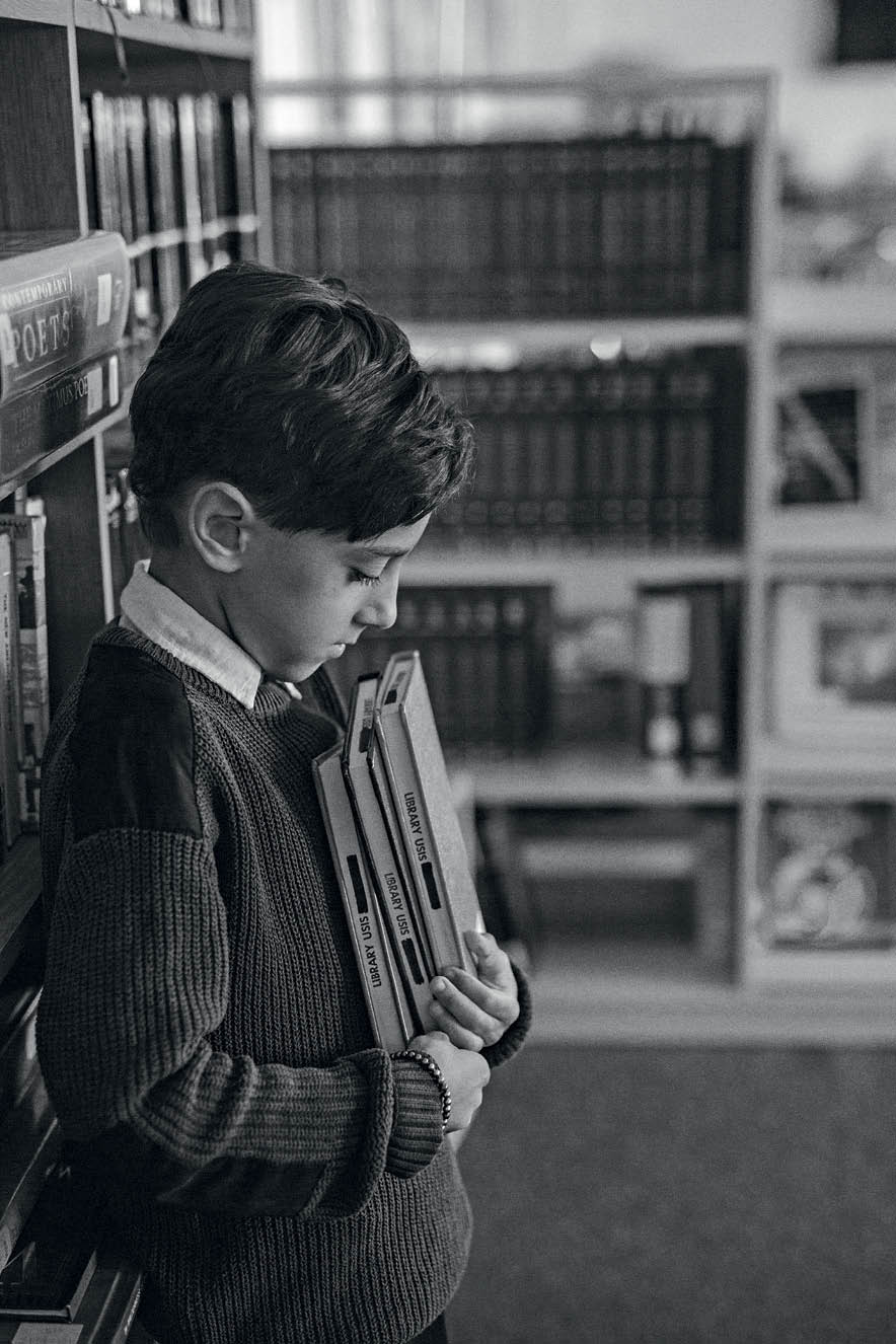 menino, com a cabeça abaixada, segurando livros
