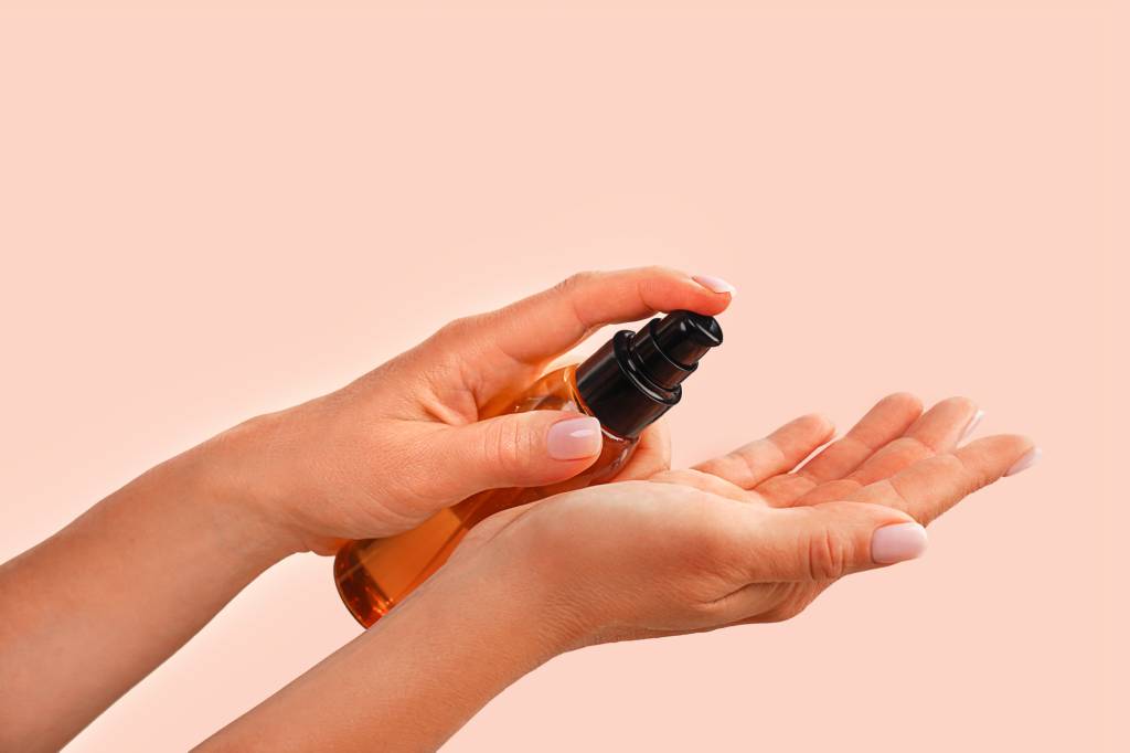 Female hands holds bottle with natural organic Face Serum or Essential Organic Oil on trendy peach pink color background Óleo capilar sendo aplicado nas mãos