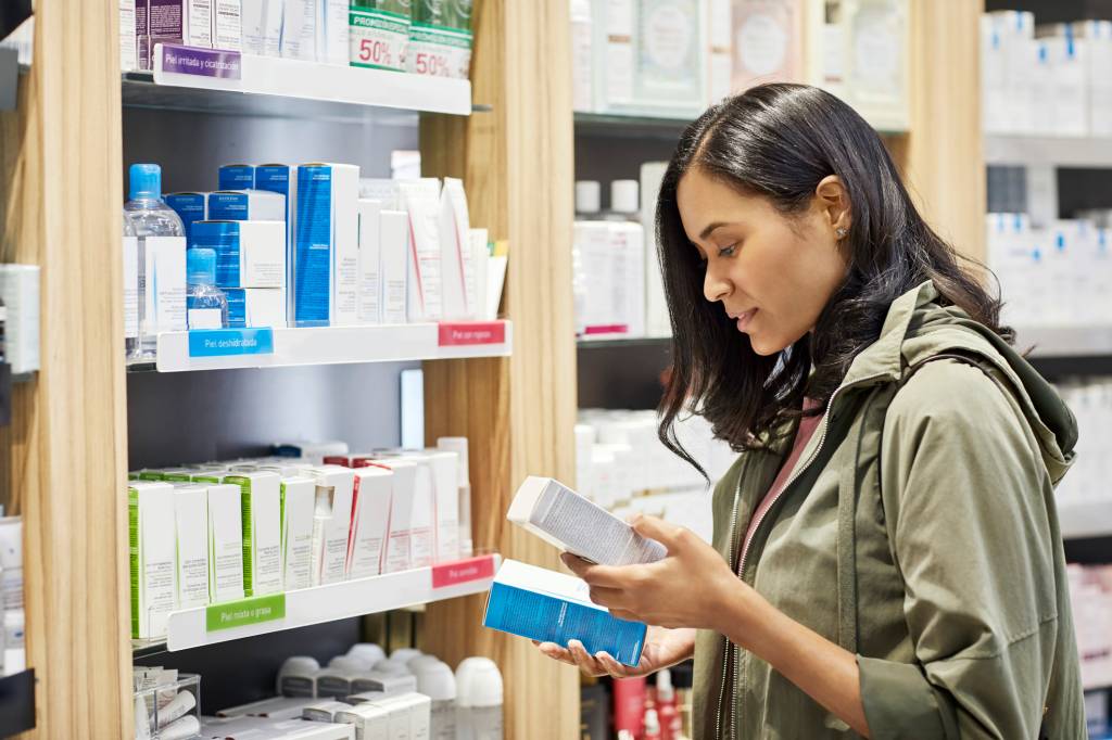 Customer comparing medicines by rack at pharmacy Mulher analisando rótulos de produtos