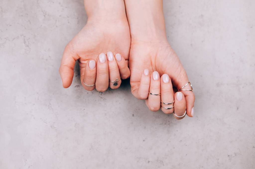 Woman hands with nude pink manicure and with many various silver rings on fingers on concrete gray background. Concept of trendy boho style. Flat lay style with copy space Unhas em fundo cinza