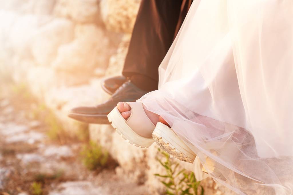 Bride and groom legs and shoes together sitting after an excited and exhausted wedding day. Noiva de plataforma