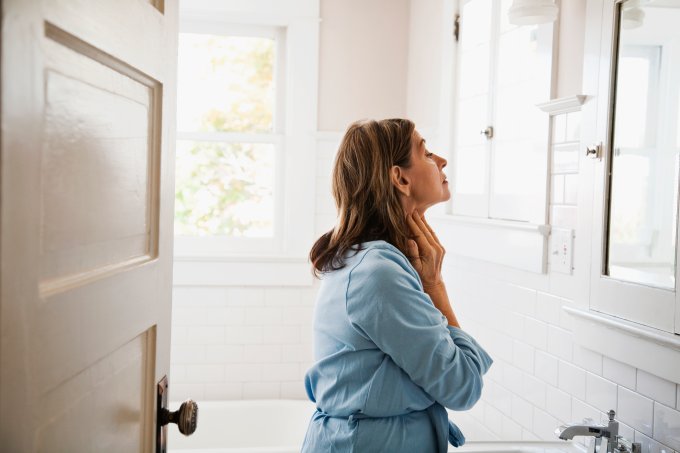 Woman looking in bathroom mirror, touching neck