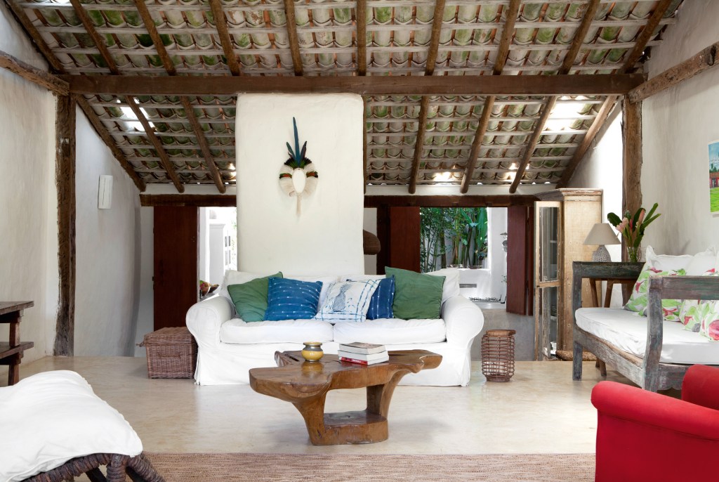 A sala de estar tem poucos móveis e permite a livre circulação. Destaque para a mesa orgânica de Hugo França, para o cocar feito por Aruê (um índio pataxó da região) e para as telhas à vista. 